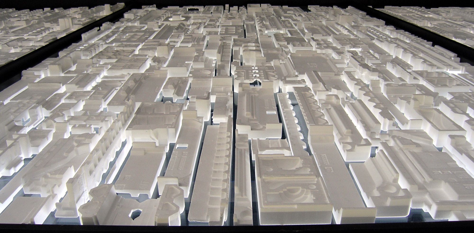Close-up of a backlit white massing model of a city, showing blocks and streets at scale