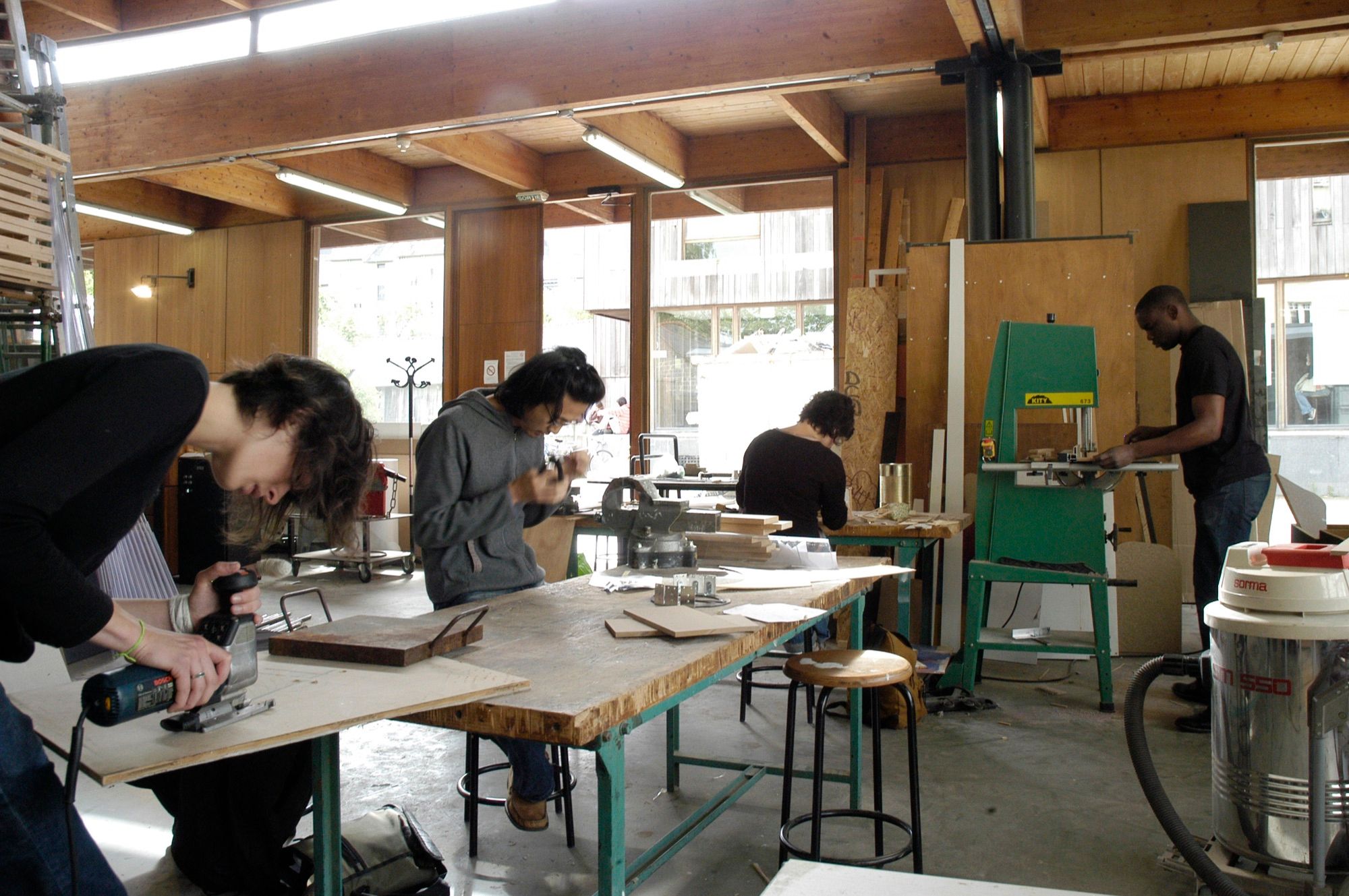Model-making workshop with people cutting parts using a jigsaw and band saw at workbenches