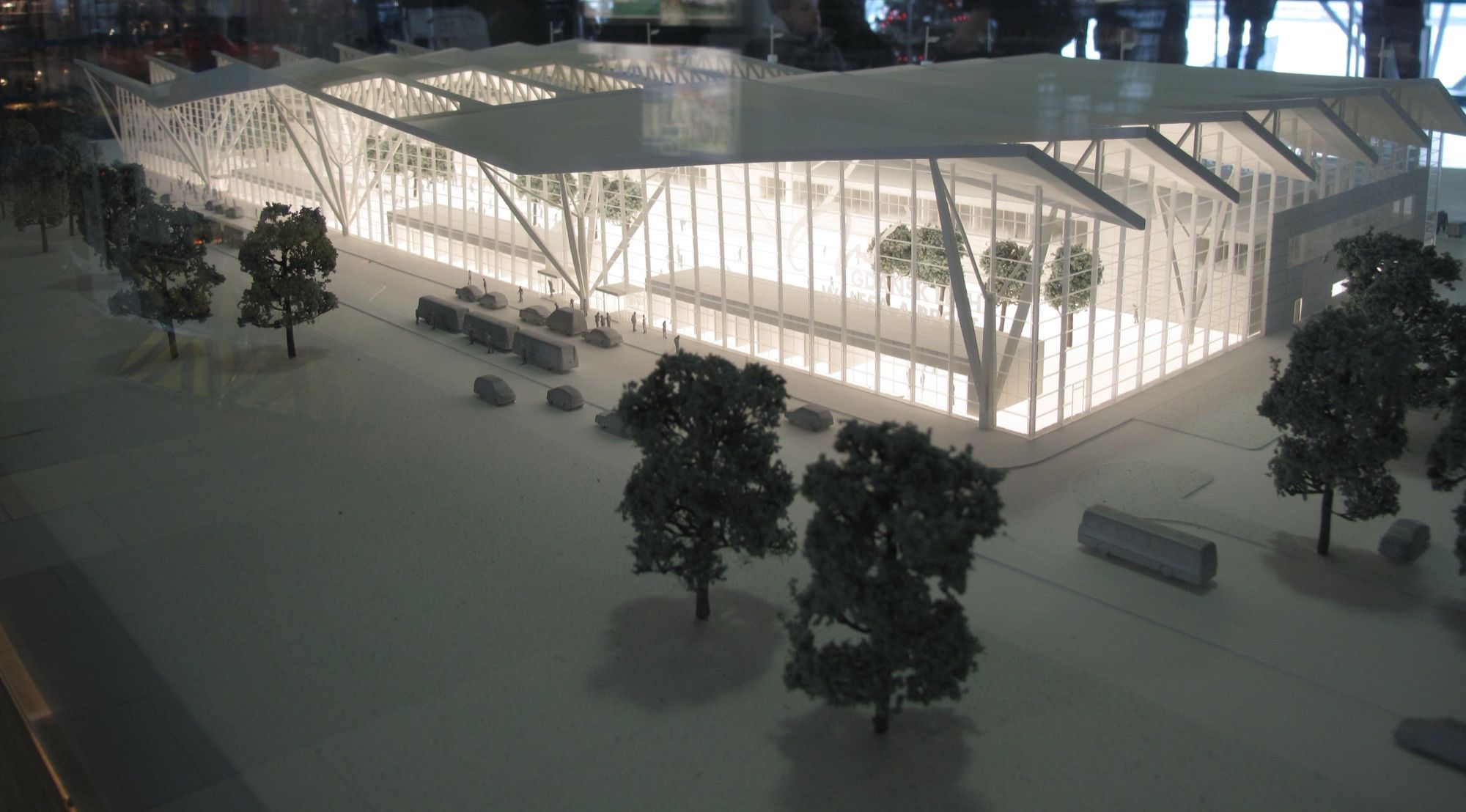 Illuminated scale model of an airport terminal with miniature trees, buses and cars